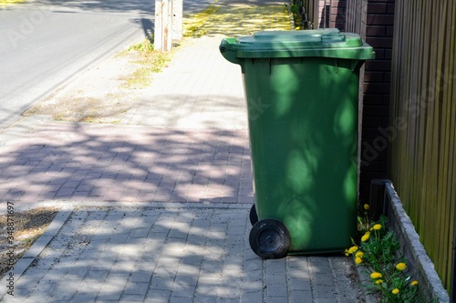 Green plastic garbage can or trash disposal bin on wheels. Trash bin on the pavement. Space for text. Garbage collection, ecology concept