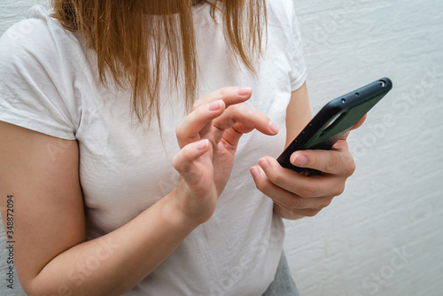 Beautiful girl makes online shopping through a smartphone on a background of a white brick wall during the caronavirus