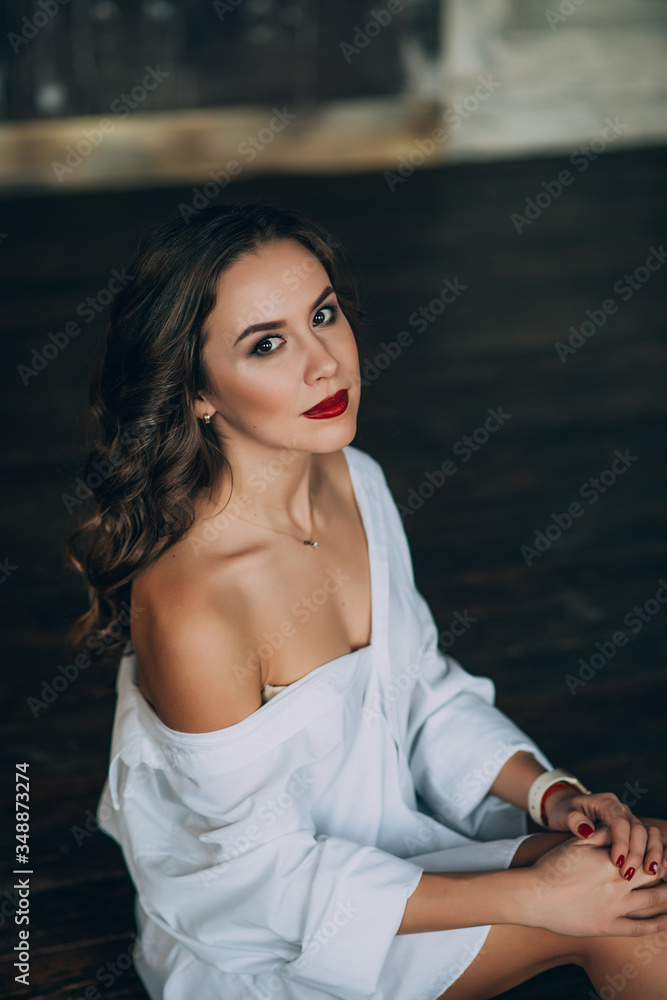 Fashionable young woman with perfect dark curly hair and beautiful make-up with puffy red lips in an unbuttoned white shirt. Soft selective focus.