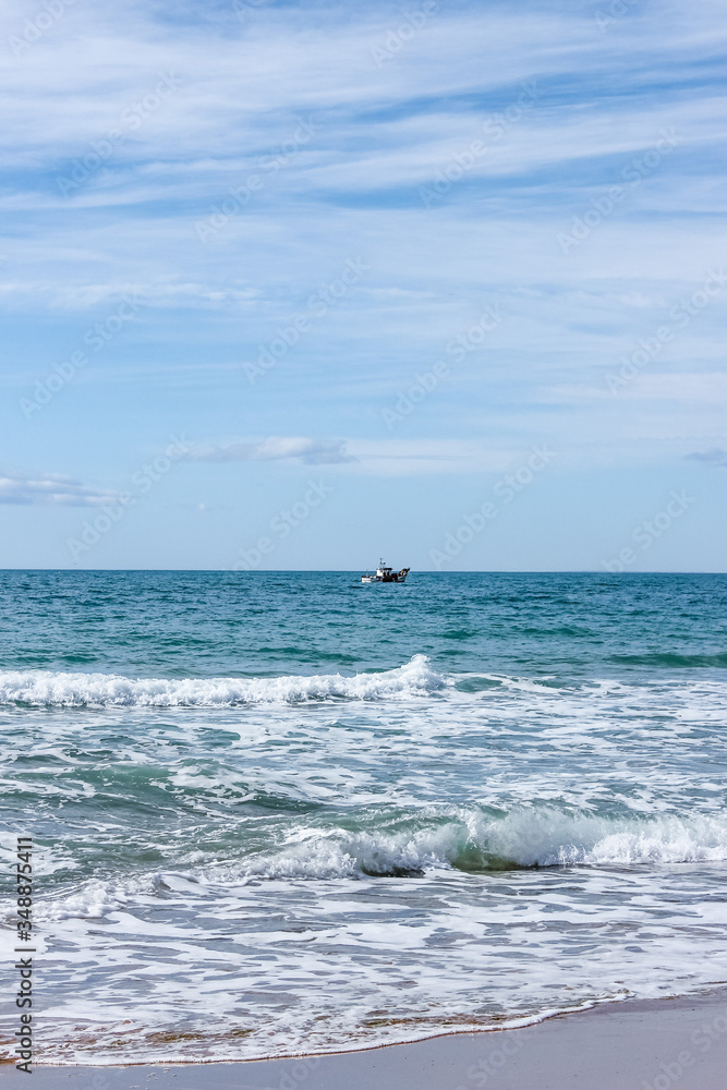 landscape with sea, beach, blue sky and  small white ship in distance, sunny day in Mediterranean