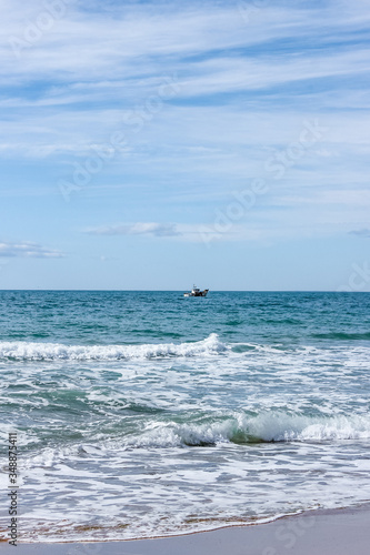 landscape with sea, beach, blue sky and small white ship in distance, sunny day in Mediterranean