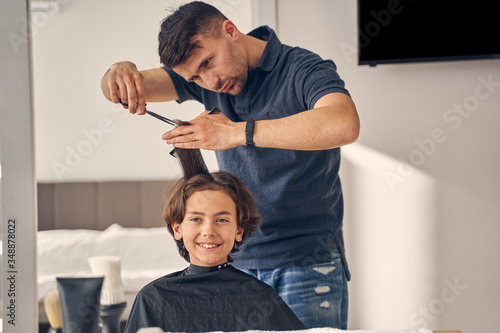 Young man carefully holding and cutting hair