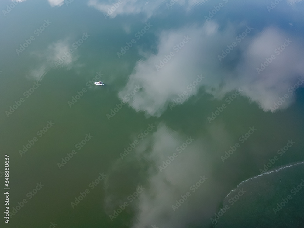 Fototapeta premium Aerial drone shot flying over fishermen in a small fishing boat on a sea. Beautiful winter landscape ocean. Aerial View. Drone shot over a beautiful lake