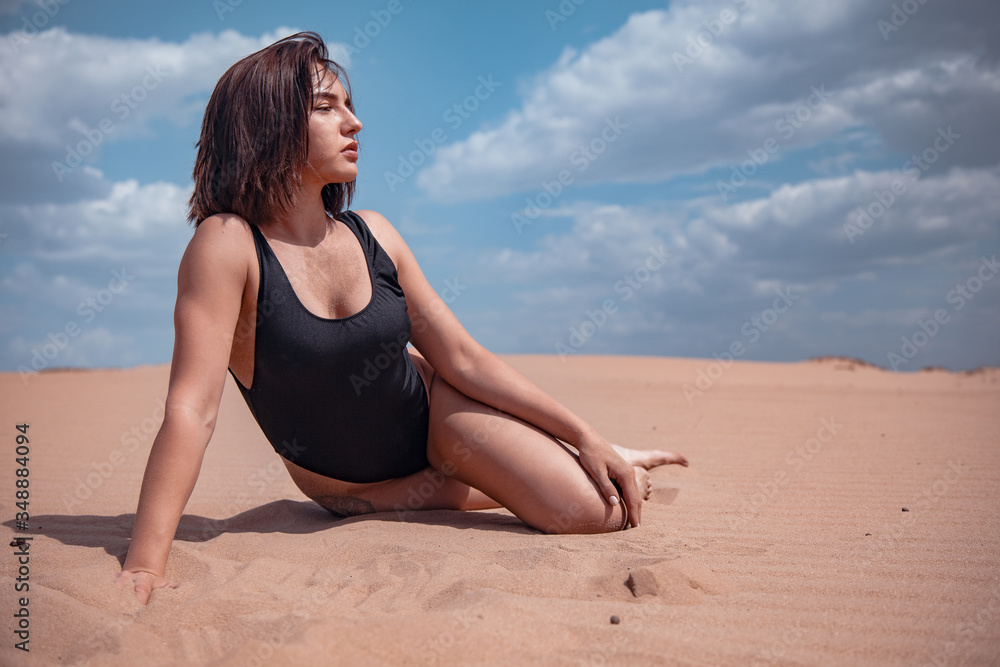 The girl in a black piece swimsuit lies on the sand in the desert