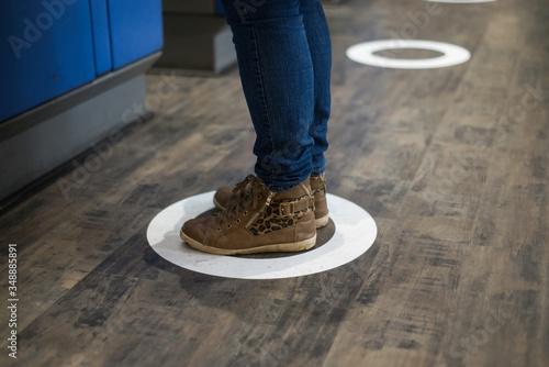 Closeup of feet of woman standing in the social distancing symbol on the floor in the train station  during the Covid-19 pandemic photo