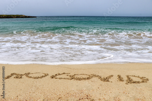 "No covid" written on the sand of the shore of a beach with incoming waves. Fear of beach resort managers for the upcoming summer season due to the coronavirus covid-19