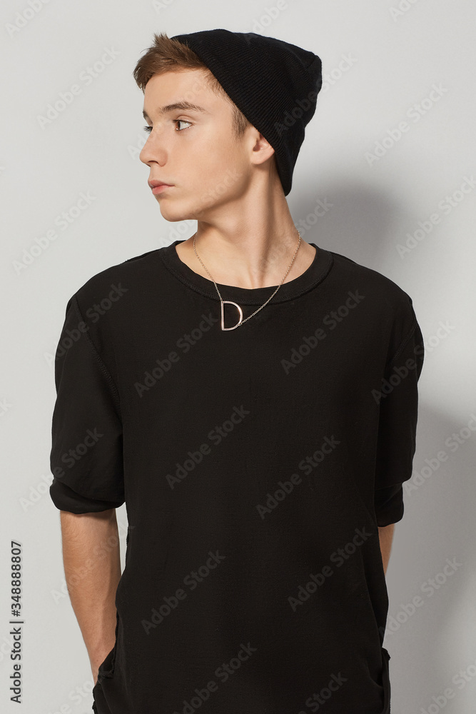 Εκτύπωση καμβά A young brown-haired man in a black watch cap and a black sweatshirt is wearing a golden necklace with a pendant in the shape of a letter D