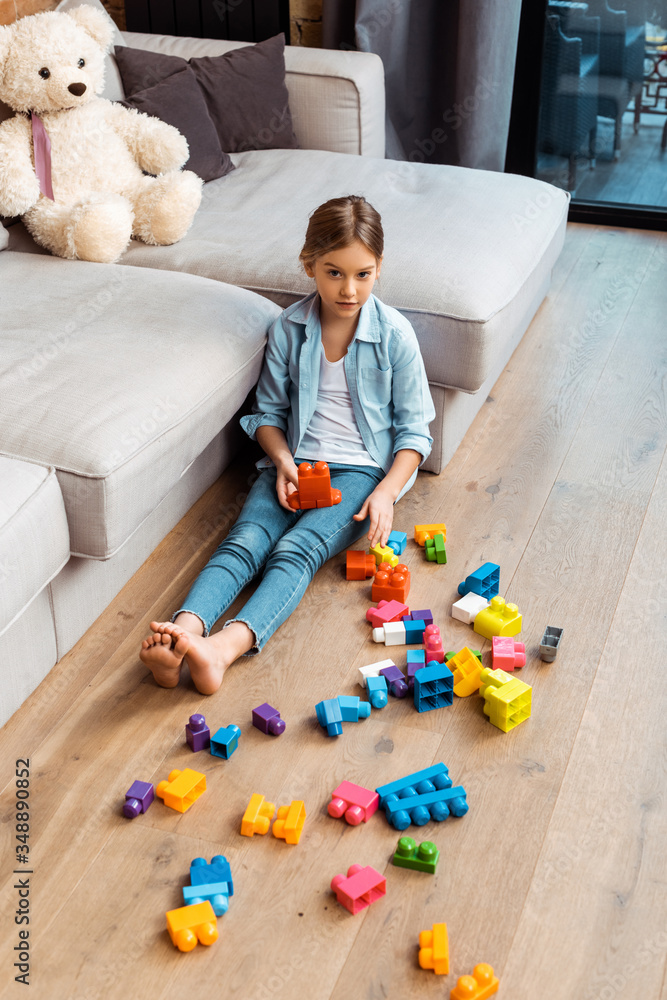 cute kid sitting on floor near building blocks and sofa cute kid sitting on floor near building blocks and sofa