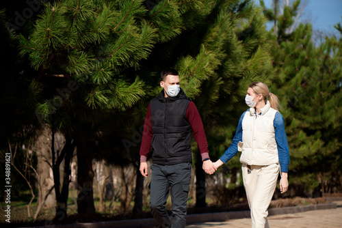 Young European man and woman in protective disposable medical mask walking outdoors afraid of dangerous NCoV 2019 influenza coronavirus mutated and spreading in China