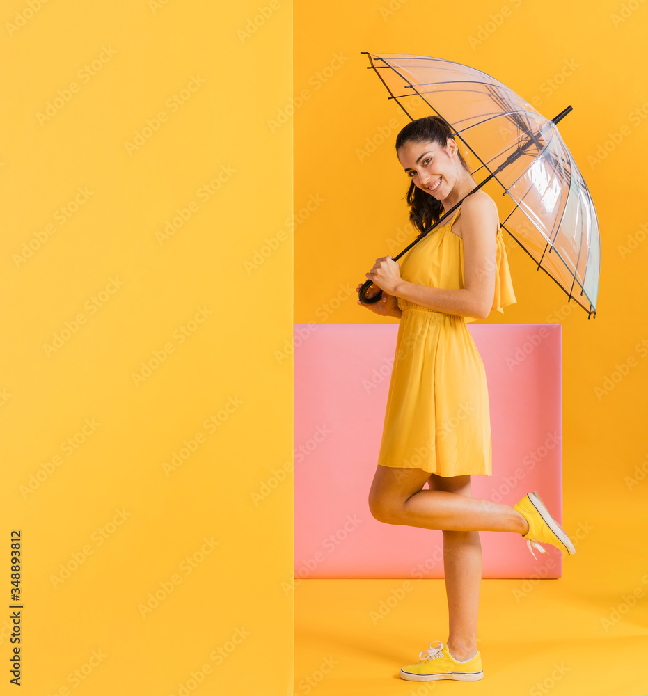Happy woman in yellow dress with a transparent umbrella. Colorful creative yellow studio background. Happy woman in yellow dress with a transparent umbrella. Colorful creative yellow studio background.