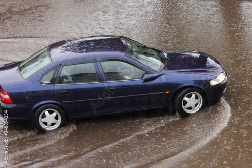 Old German dark blue sedan car drives slowly through a large puddle  heavy rain in the city