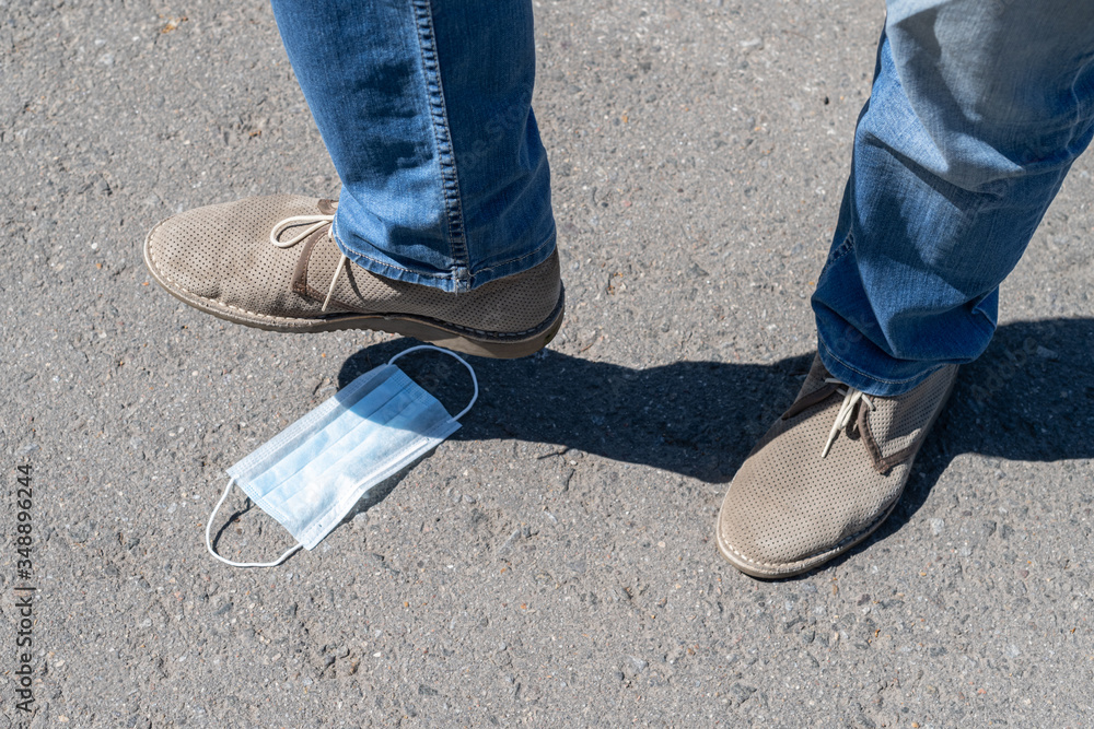 A man steps on a medical mask lying on the asphalt. Over coronavirus. End of pandemic and quarantine. End of the epidemic. Concept A man steps on a medical mask lying on the asphalt. Over coronavirus. End of pandemic and quarantine. End of the epidemic. Concept