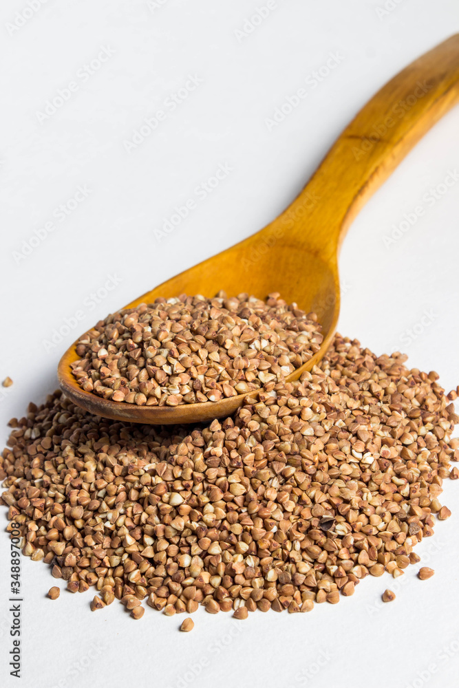 a handful of buckwheat and a wooden spoon above it. There is not much buckwheat on the spoon. Photo on a white background a handful of buckwheat and a wooden spoon above it. There is not much buckwheat on the spoon. Photo on a white background