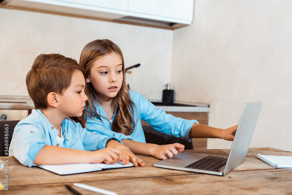 selective focus of sister and brother looking at laptop while e-learning at home selective focus of sister and brother looking at laptop while e-learning at home