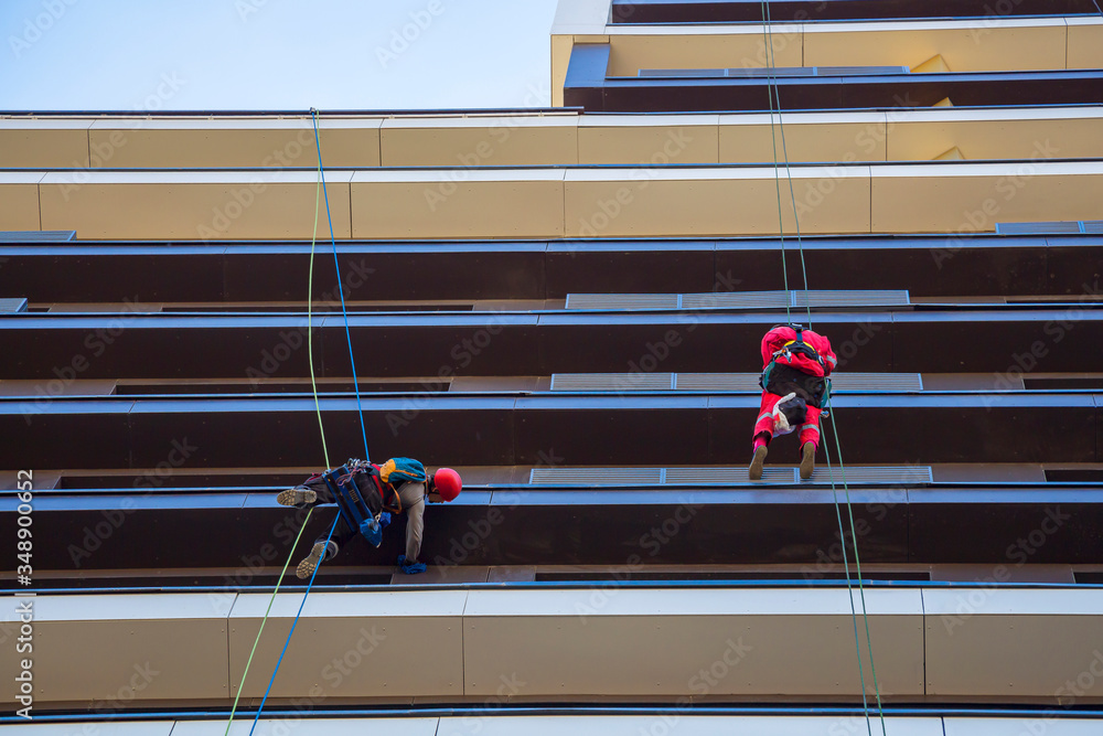 Two climber washing windows and glass facade of the high-rise or skyscraper. Window washer profession. Cleaning service concept. Artificial noise compression, selective focus