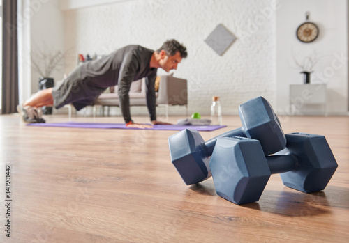 Strong sportive man doing exercises at home, close up dumbbell, sport mat, decorative background living room concept.