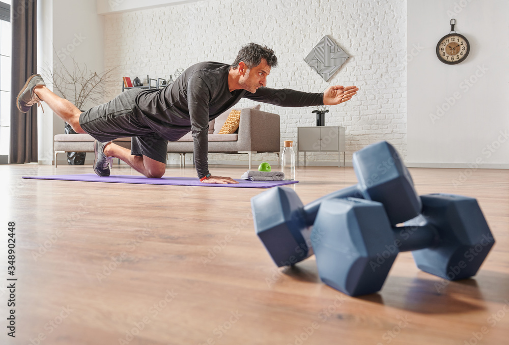 Strong sportive man doing exercises at home, close up dumbbell, sport mat, decorative background living room concept. Strong sportive man doing exercises at home, close up dumbbell, sport mat, decorative background living room concept.