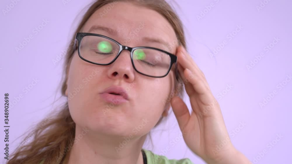 Very tired young woman wearing glasses makes the gesture of mopping her brow and fetching her breath. Concept of working hard, household duties or other exhausting job. Indoors, lilac background Very tired young woman wearing glasses makes the gesture of mopping her brow and fetching her breath. Concept of working hard, household duties or other exhausting job. Indoors, lilac background