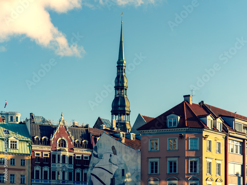 Facades of old houses on the Dome Square against the background of the spire of the Peter Cathedral in Riga. Panorama of two frames.