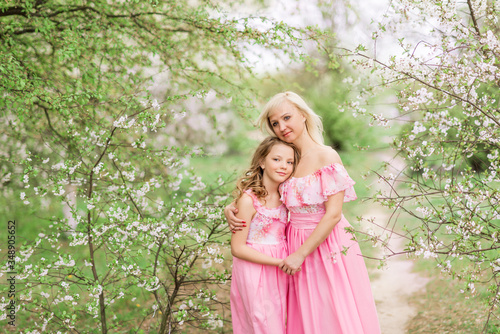 Mother and daughter in pink dresses in a blooming garden in spring.