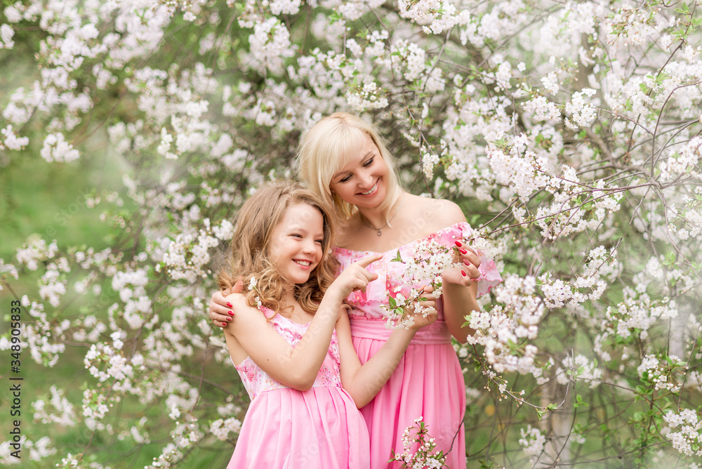 Mother and daughter in pink dresses in a blooming garden in spring. Mother and daughter in pink dresses in a blooming garden in spring.