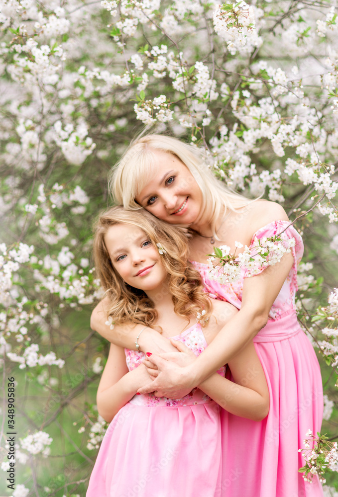 Mother and daughter in pink dresses in a blooming garden in spring. Mother and daughter in pink dresses in a blooming garden in spring.