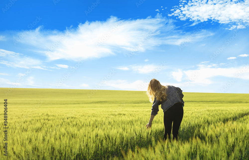 Blonde girl through the green wheat field and blue sky with white clouds. Concept of travel, inspiration, freedom, lifestyle with copy space. Blonde girl through the green wheat field and blue sky with white clouds. Concept of travel, inspiration, freedom, lifestyle with copy space.
