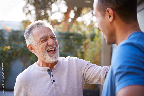 Senior Hispanic Man Talking And Laughing With Adult Son In Garden At Home
