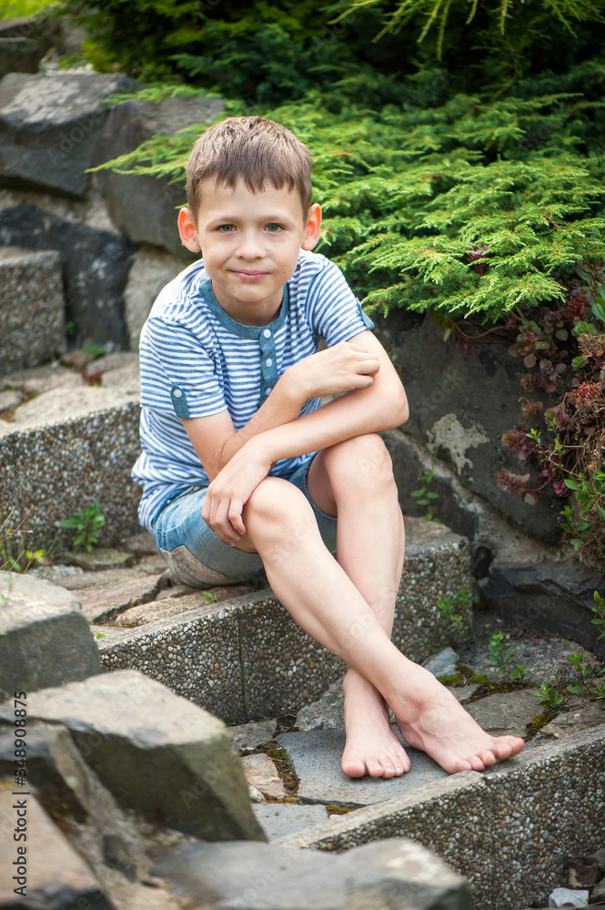 A boy of 8 years old is sitting on a stone staircase with bare feet in shorts. A boy of 8 years old is sitting on a stone staircase with bare feet in shorts.