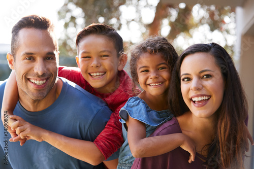 Portrait Of Smiling Hispanic Family With Parents Giving Children Piggyback Rides In Garden At Home photo