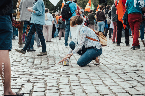 Young woman wearing a protective face mask is kneeling on the ground grabbing a bucket containing chalk after writing a political message on the ground during a demonstration against hate speech.