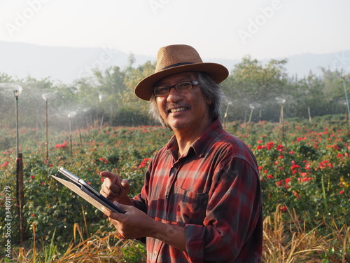 Asian farmer old man or gardener using touch screen monitor in Digital Tablet.Water sprinkler on Intelligent agriculture system have high tech technology  for modern organic farm.