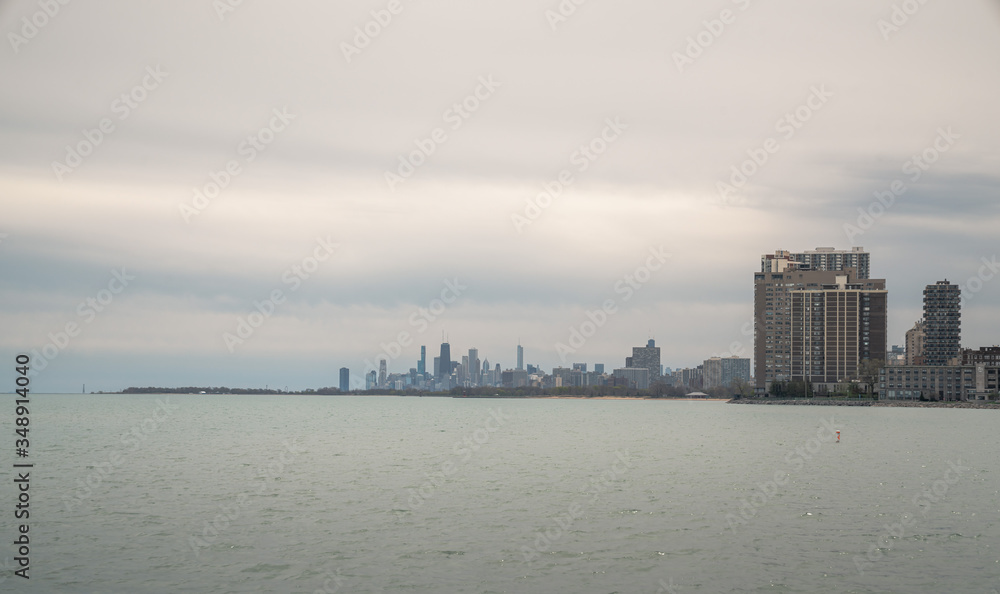 Panoramic cityscape view of the City of Chicago skyline from Loyola park on the north side with the water of Lake Michigan in the foreground and cloudy gray sky above in springtime.