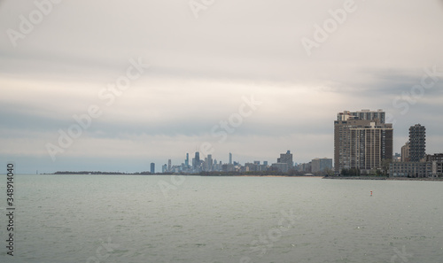 Panoramic cityscape view of the City of Chicago skyline from Loyola park on the north side with the water of Lake Michigan in the foreground and cloudy gray sky above in springtime.