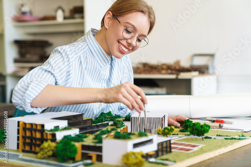 Photo of joyful young woman architect designing draft with house model