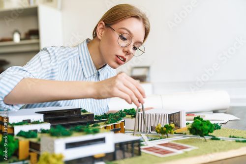 Photo of focused young woman architect designing draft with house model