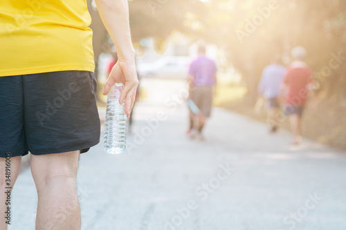 Man holding a bottle of water on the background of runner. Concept of training in the outdoor and a good life. 