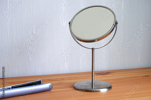 On a wooden table-a mirror and an iron for straightening hair. Suitable for mockups and advertising backgrounds.