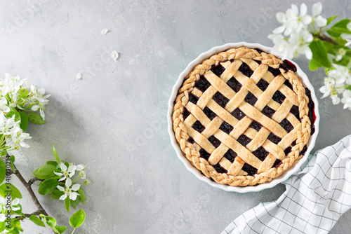 Cherry, red berry pie in baking dish on Gray background with flowers. Top view. Copy space. Bakery background, homemade pastry recipe, menu