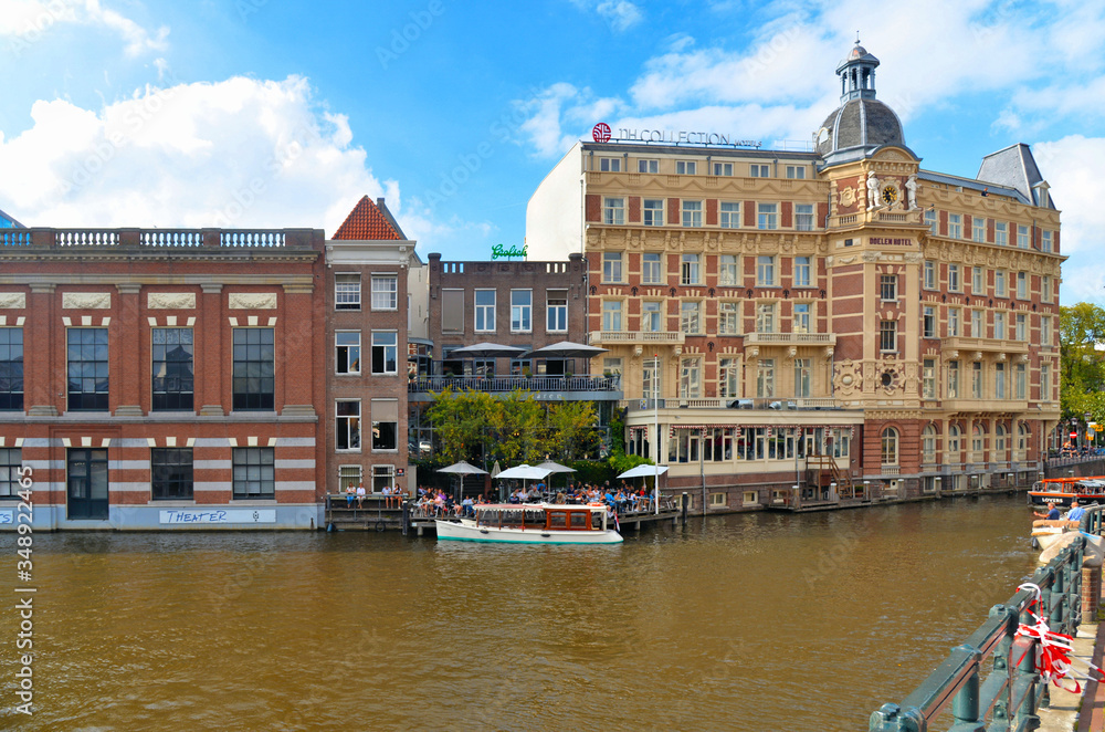 Cityscape with canal in Amsterdam city. Picturesque town landscape with people and old buildings facade in Netherlands with view on river Amstel.