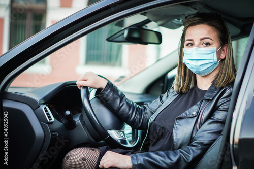 Young woman driving car with protective mask on her face. 