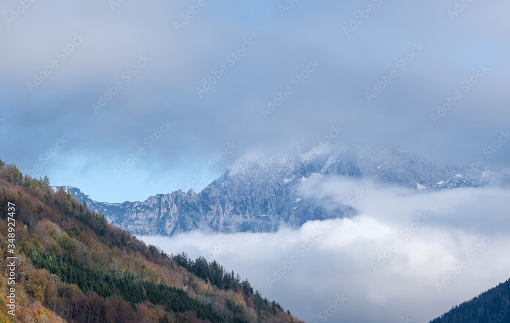 Overcast autumn alpine view with famous Bavarian mount Watzmann silhoette fragments through fog and clouds, Berchtesgadener Land, Bavaria, Germany. Climate, environment and weather sky background