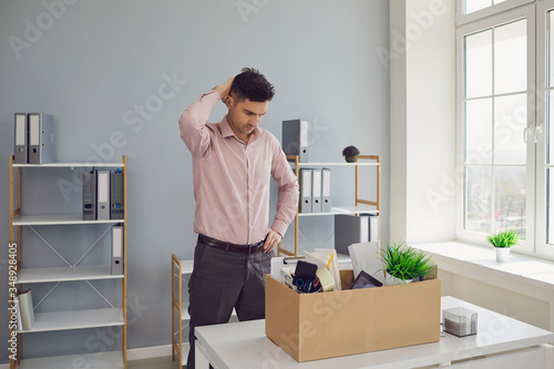 Unemployment. Dismissal. Dismissed businessman is upset with a cardboard box holding his head in his hands while sitting in a company office.
