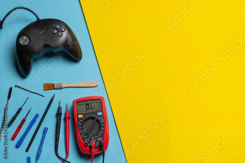 Multimeter, tools and gamepad over blue and yellow background. Concept of diagnosis and technical assistance in electronics and video games. concept of repair and maintenance of amusement machines