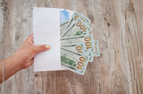 white envelope with dollars in hand on a wooden background.