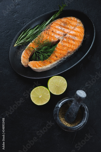 Black plate with roasted salmon steak, high angle view over black stone background, vertical shot, selective focus