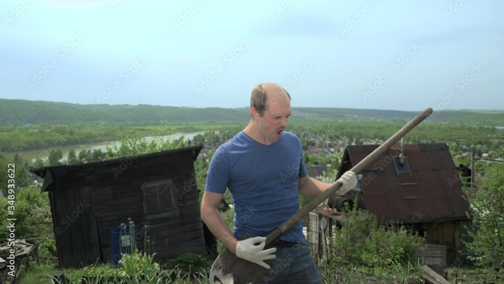 funny balding man imitates playing a guitar with a shovel on a farm funny balding man imitates playing a guitar with a shovel on a farm