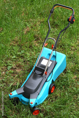 Electric lawn mower stands on green unmown grass in cloudy weather