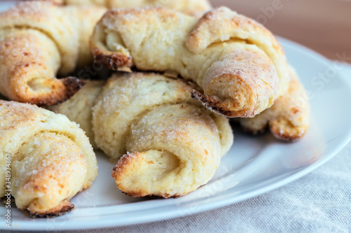 Croissants from a cottage cheese dough on a white plate on a gray linen tablecloth just taken out of the oven. The process of making curd bagels or croissants. Selective focus. Closeup view