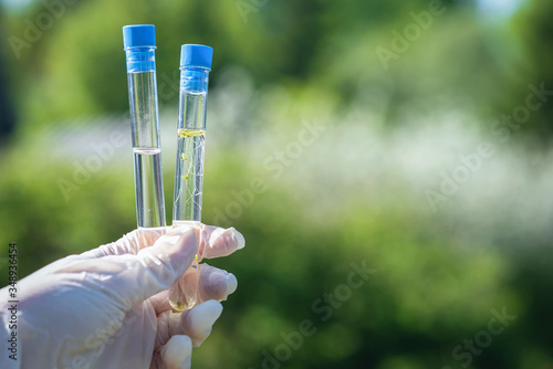 Scientist is holding in hands a clear and dirty water test tubes close up.